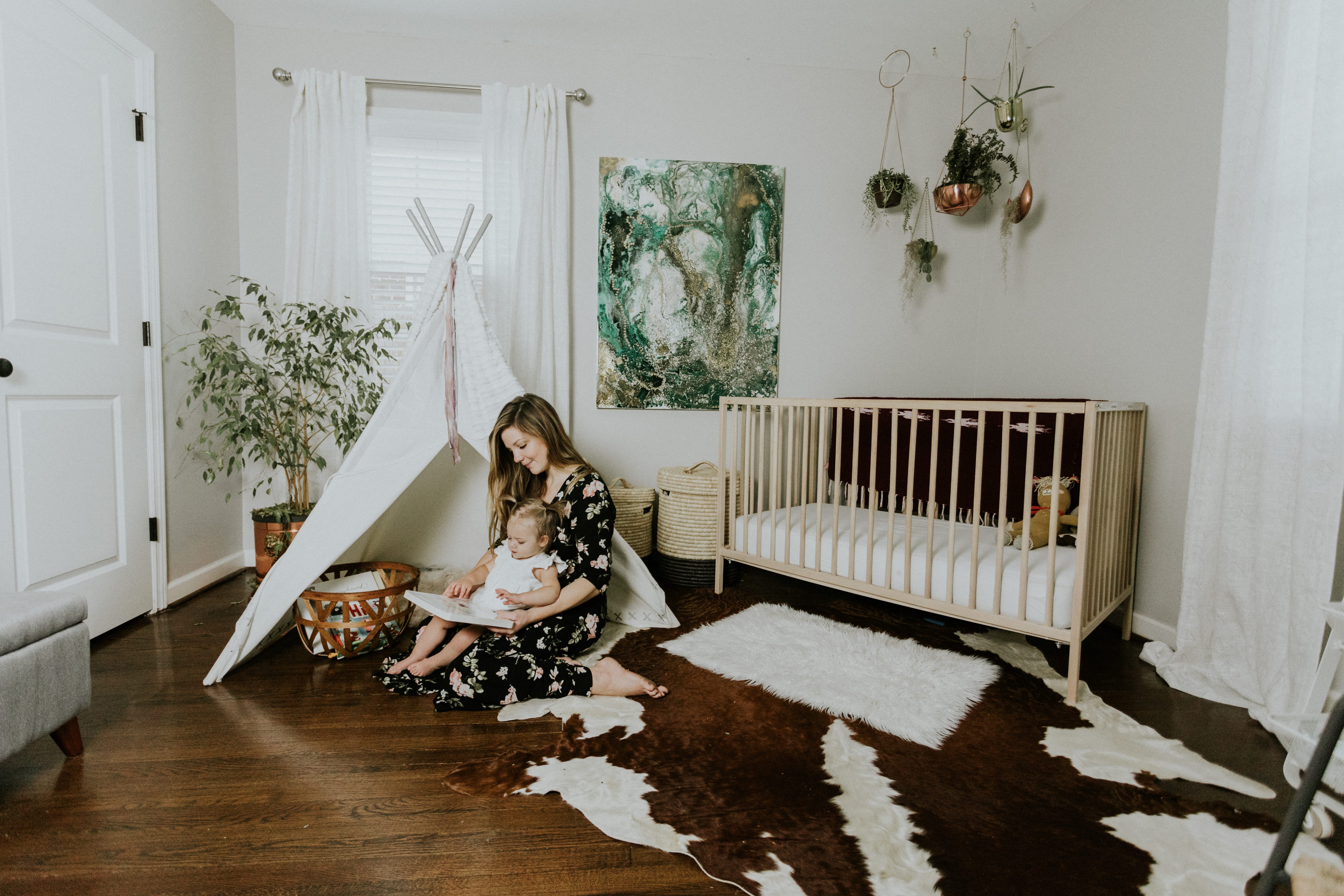 Mommy and daughter having story time in front of the Modern Nursery Land of Nod tee pee and crib.